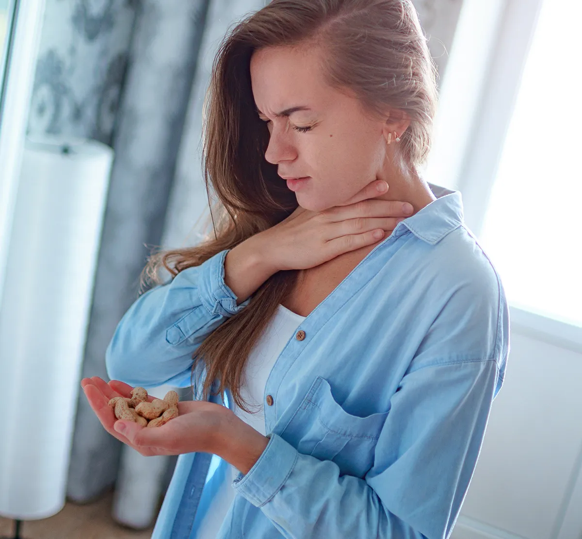 Allergie Selbsttest Allergene Stoffe im Umfeld Eine Frau mit leicht gequältem Gesichtsausdruck und mit Erdnüssen in der einen Hand und mit der anderen sich an den Hals greifend