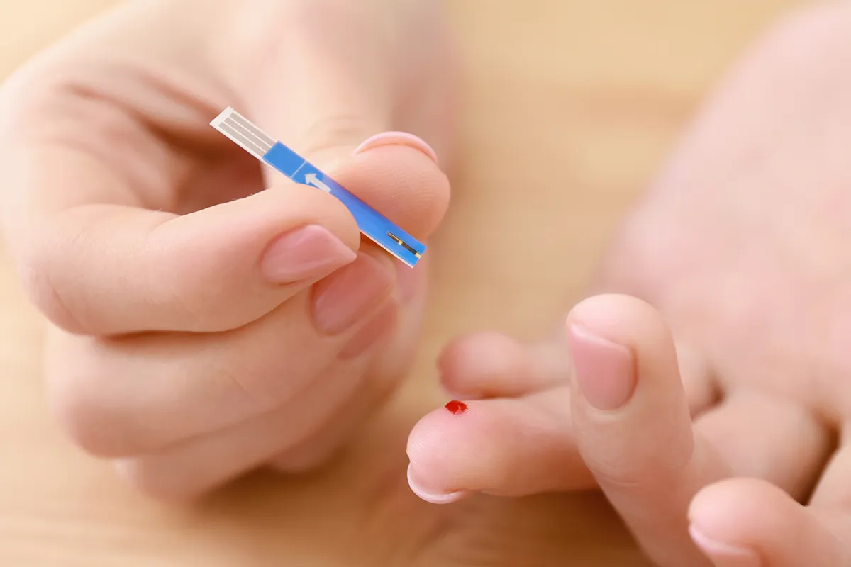 allergie-selbsttest-bluttest Großaufnahme eines blutenden Fingers einer Hand mit einem Teststreifen in der anderen Hand