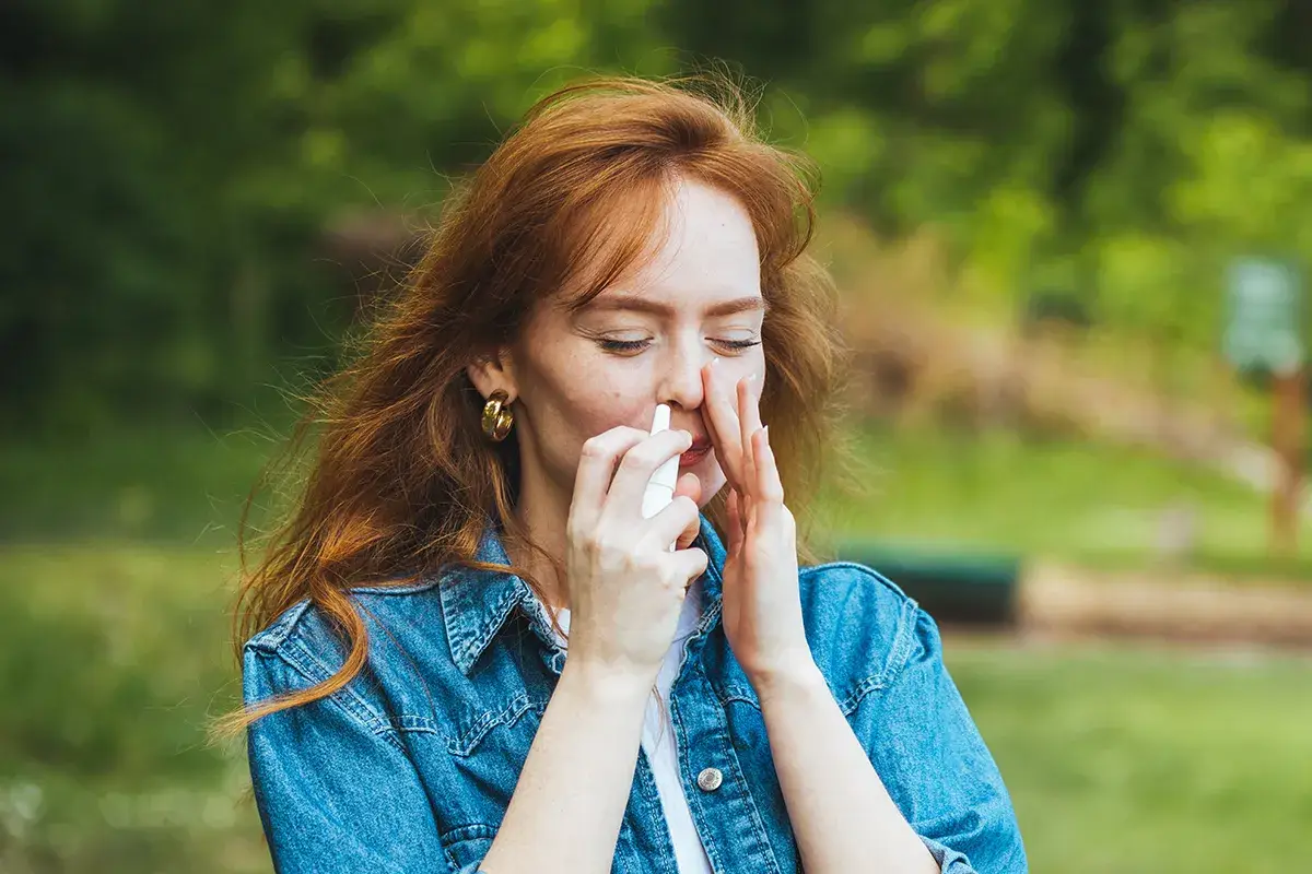 Anleitung Nasenspray bei Heuschnupfen Eine Frau wendet im grünen ein Nasenspray an