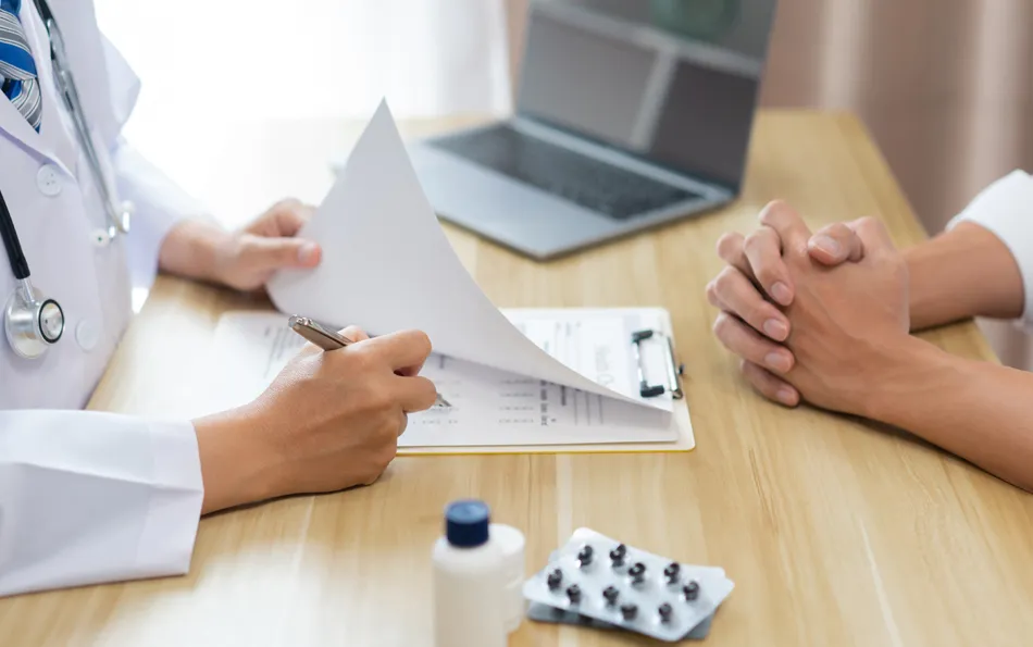 Arzt fragen unklare Testergebnisse Arzt mit Checkliste vor sich und Patient auf der anderen Seite des Tisches. Medikamente sind im Vordergrund, ein Laptop im Hintergrund