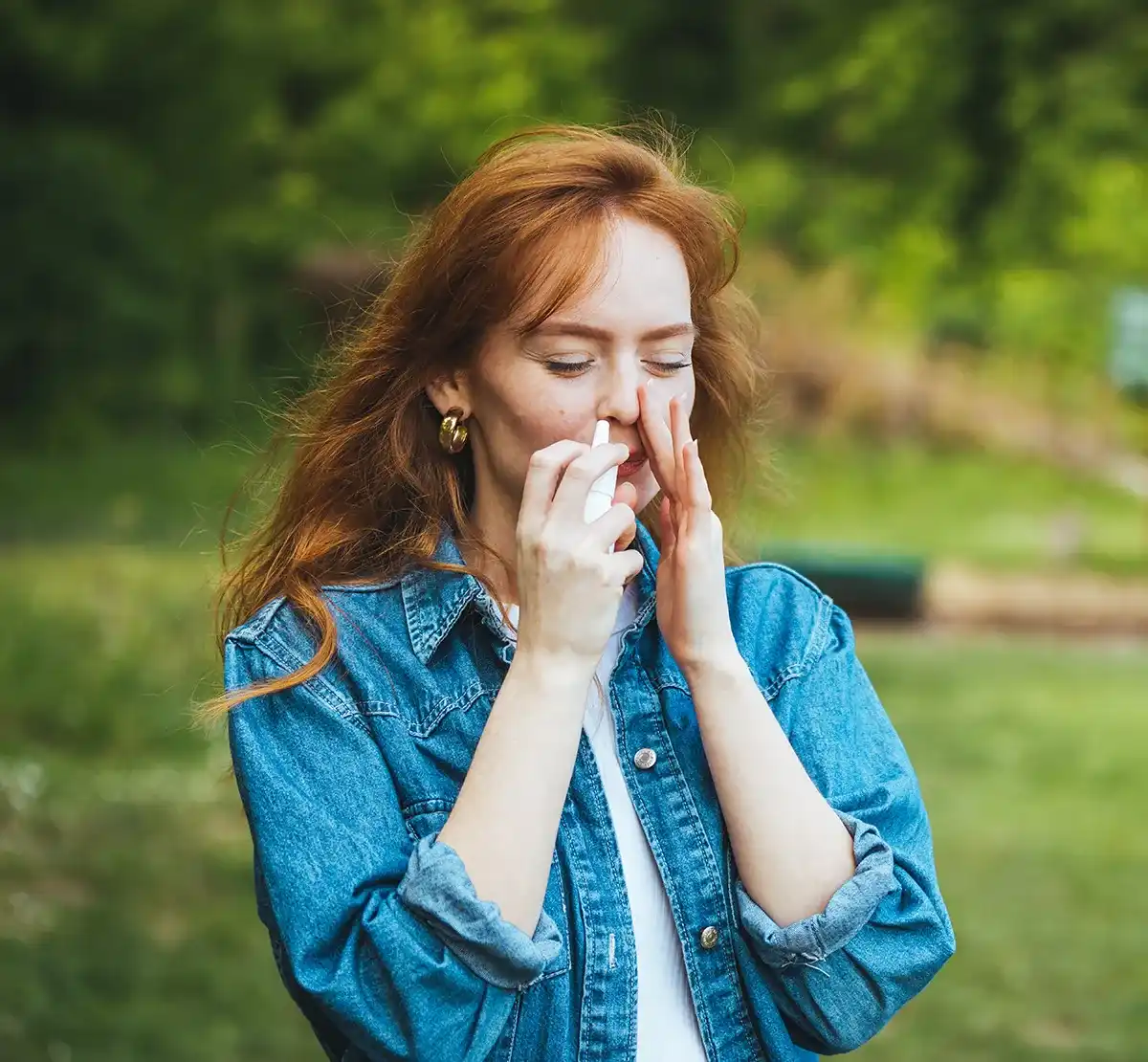 Birkenpollenallergie Behandlung Nasenspray Eine Frau wendet im grünen ein Nasenspray an