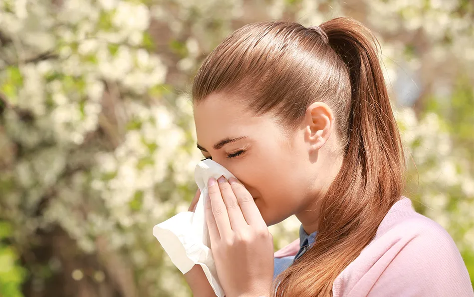 Heuschnupfen Pollenallergien Übersicht Eine Frau putzt sich vor einer blühenden Pflanze die Nase