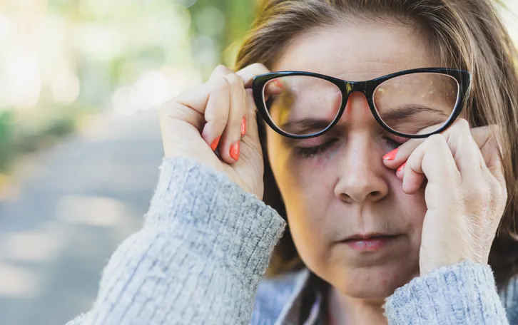Eine Frau mit Brille reibt sich darunter die drum herum geröteten Augen