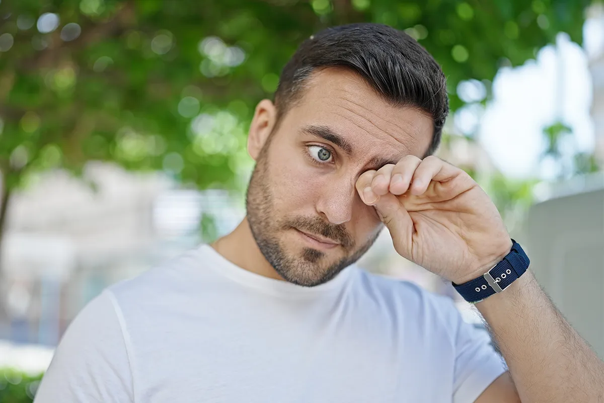 Heuschnupfen juckende Augen Ein Mann reibt sich vor einem Baum das Auge