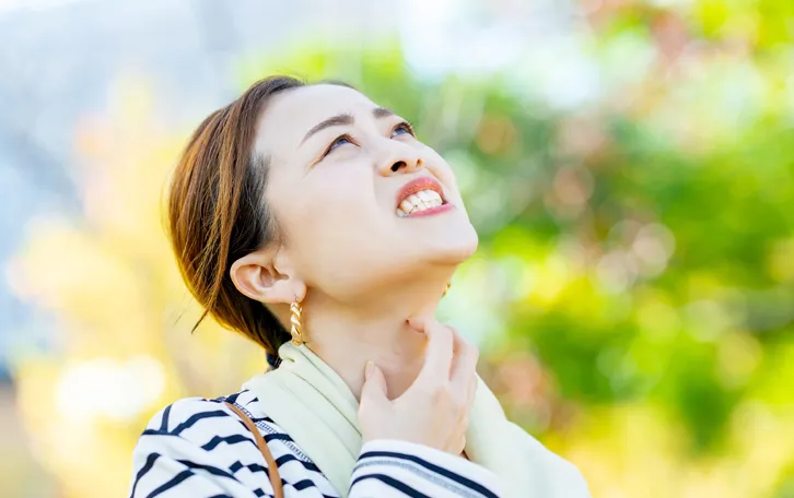 Ein Frau mit gequältem Gesichtausdruck kratzt sich am Hals