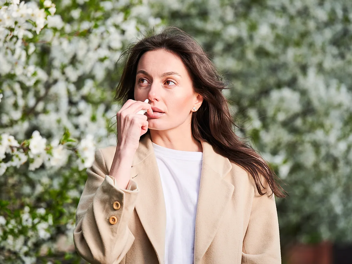 Heuschnupfen Nasenspray Vorteile Eine Frau verwendet ein Nasespray vor einer blühenden Pflanze