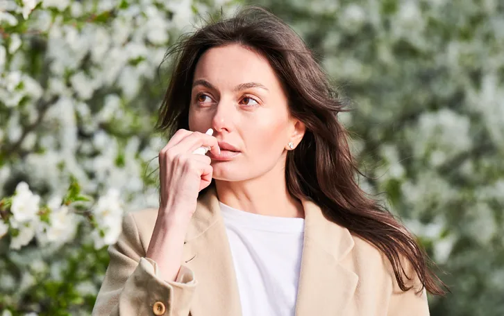 Eine Frau verwendet ein Nasespray vor einer blühenden Pflanze