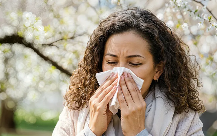 heuschnupfen-symptom-laufende-verstopfte-nase Eine Frau putzt sich vor einem blühenden Baum die Nase