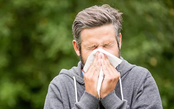 Ein Mann putzt sich mit geschlossenen Augen in der Natur die Nase
