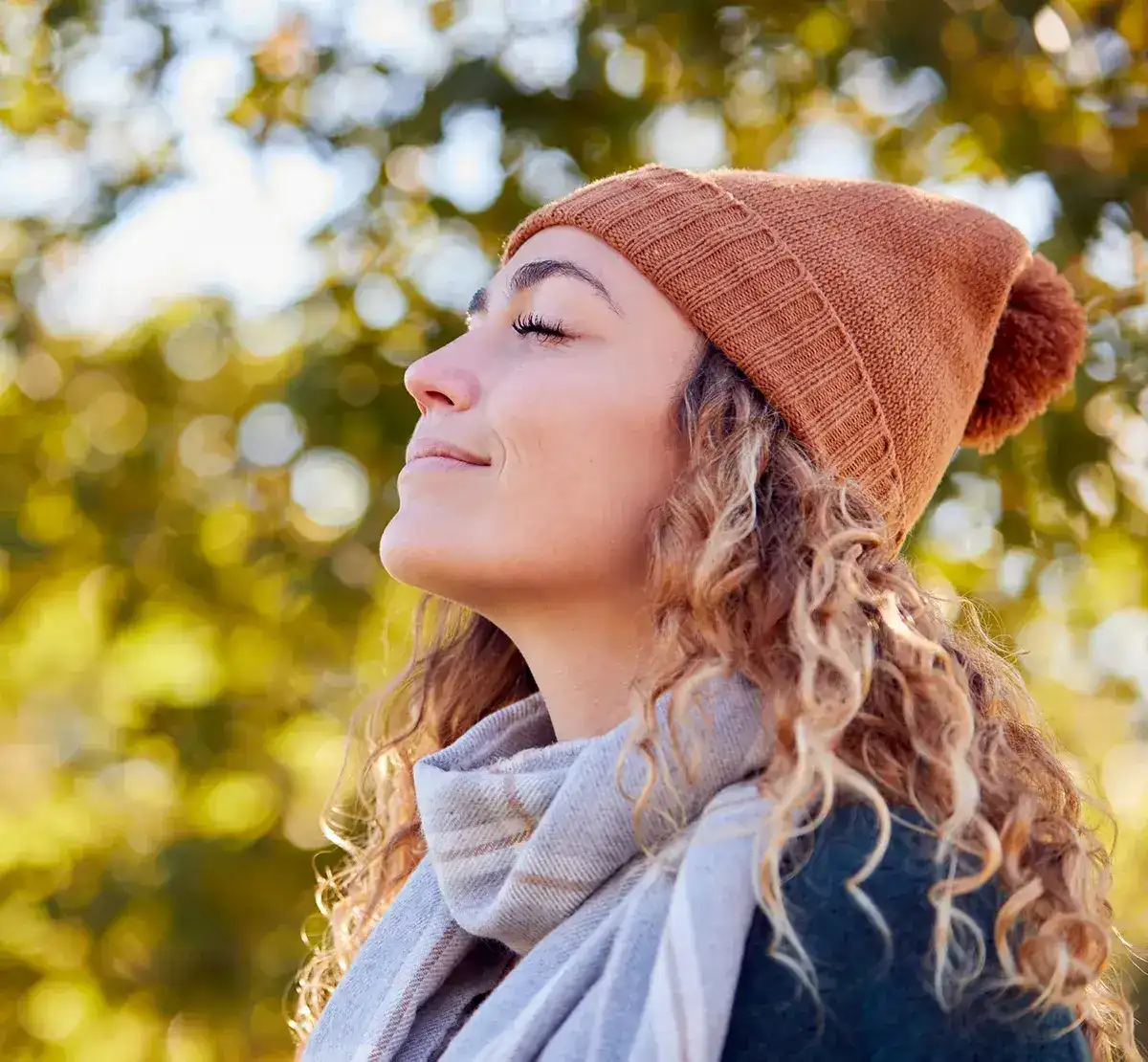 Heuschnupfenmittel lindern Symptome Eine Frau steht mit geschlossenen Augen lächelnd in der Natur mit einer Mütze auf dem Kopf
