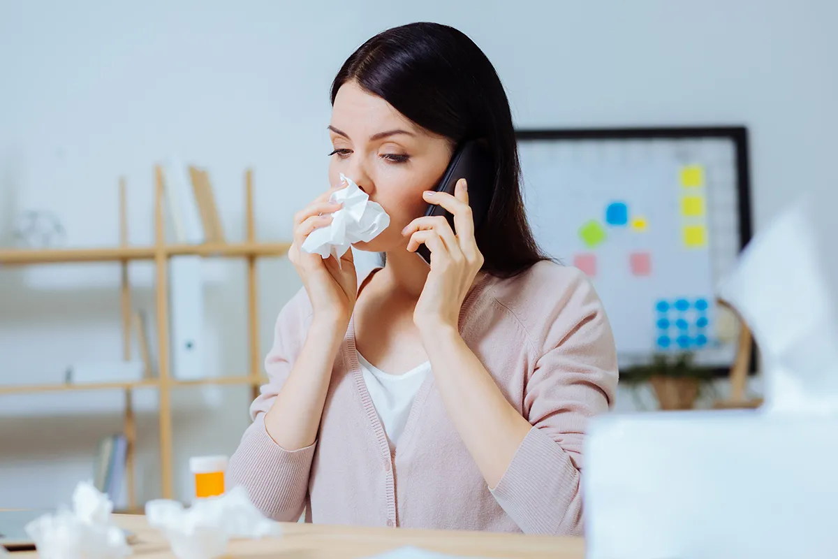 Heuschnupfenmittel Telefonberatung Frau am Telefon mit Taschentuch vor der Nase und Medikamenten vor sich