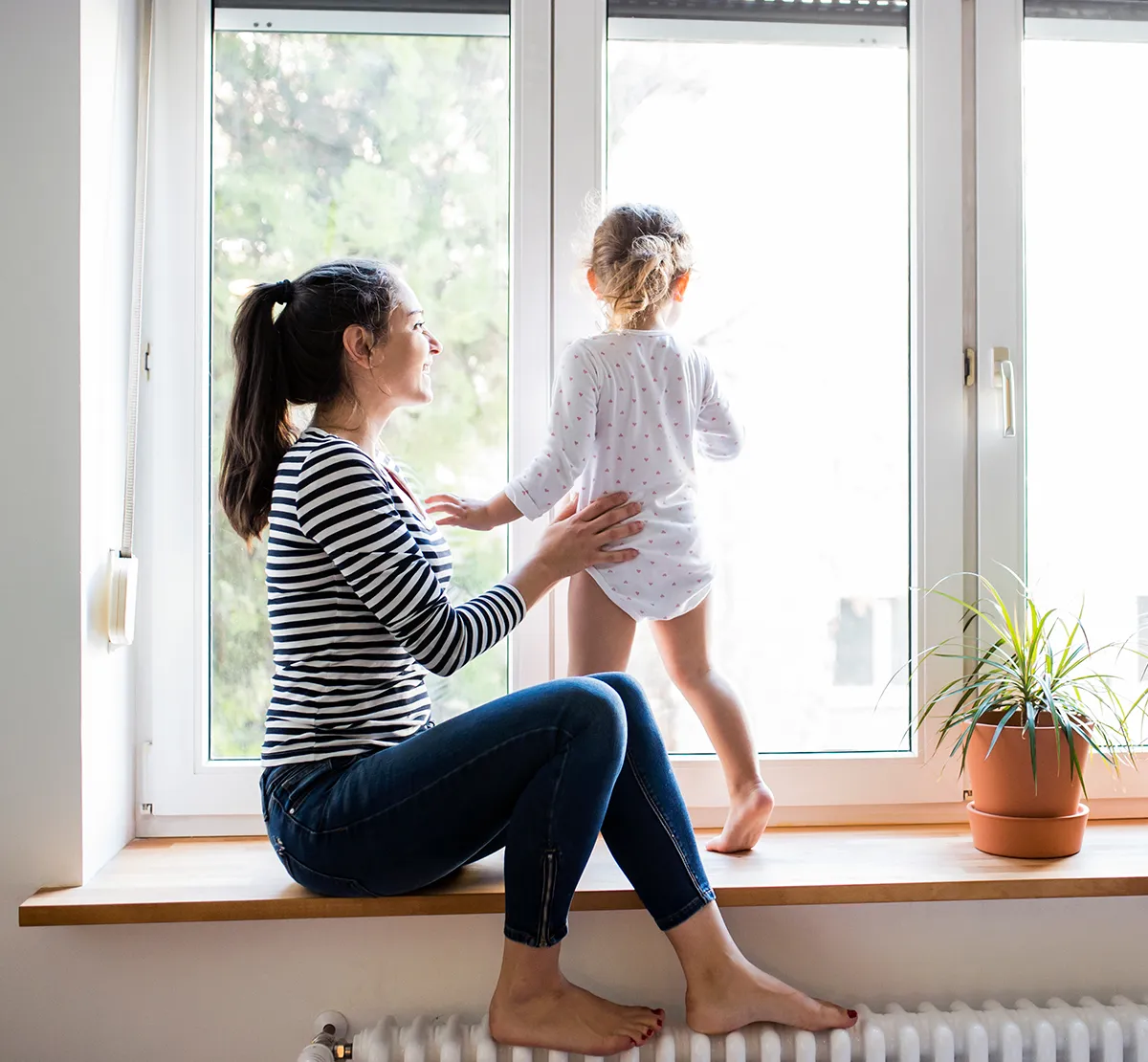 Hohe Pollenbelastung Fenster zu Frau mit Kleinkind aug einer Fensterbank