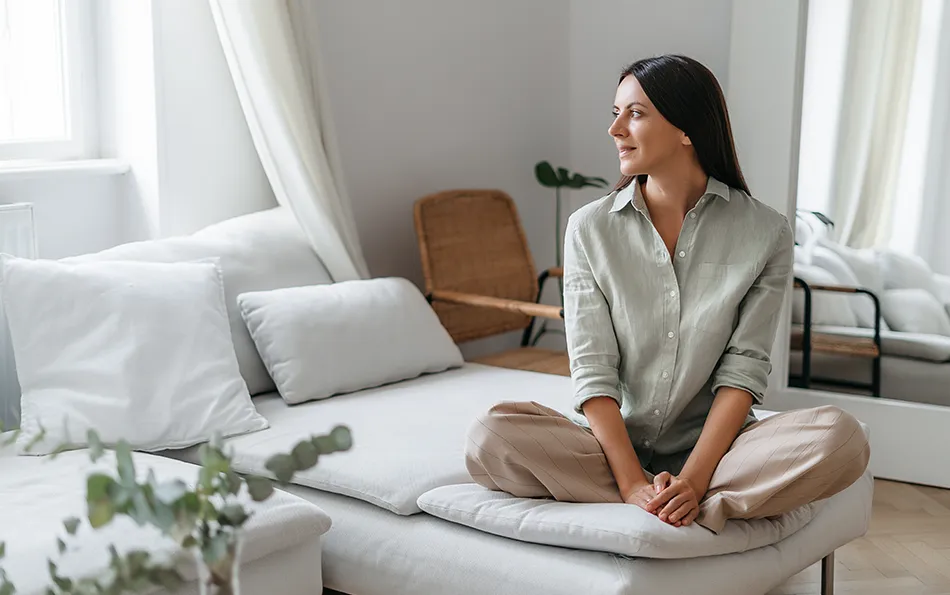 Pause bei Erkältung und Allergie Eine Frau in einem hellen Zimmer auf der Couch sitzend
