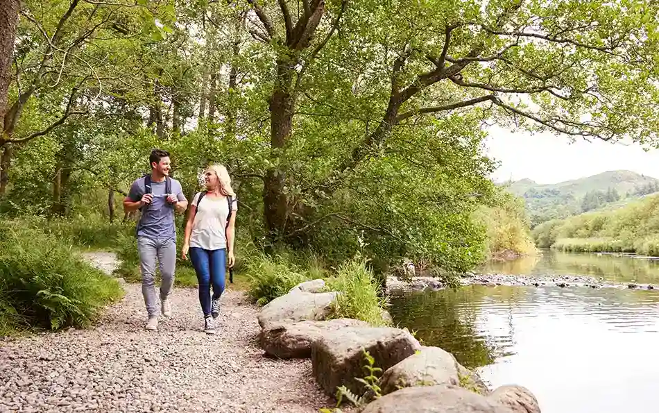Pollenarme Strecken wählen Ein Paar, welches an einem Gewässer einen steinigen Pfad unter Bäumen entlang geht