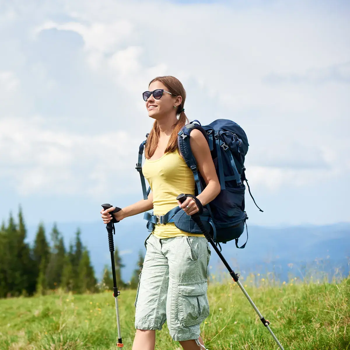 Pollenflugzeit und Ausdauersport wandern Eine lächelnde Frau mit Sonnenbrille und Wanderrucksack/-stöcken in den den Bergen