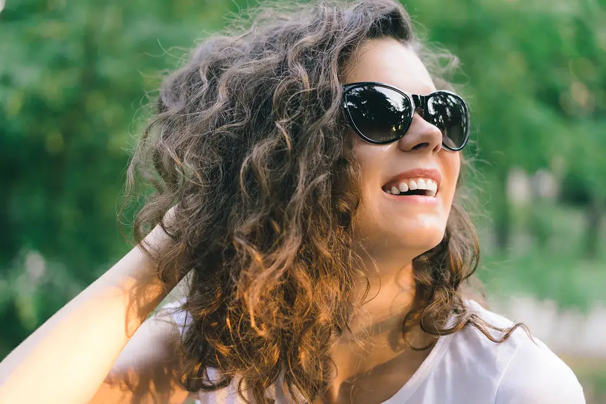 Lachende Frau in der Natur mit Sonnenbrille auf