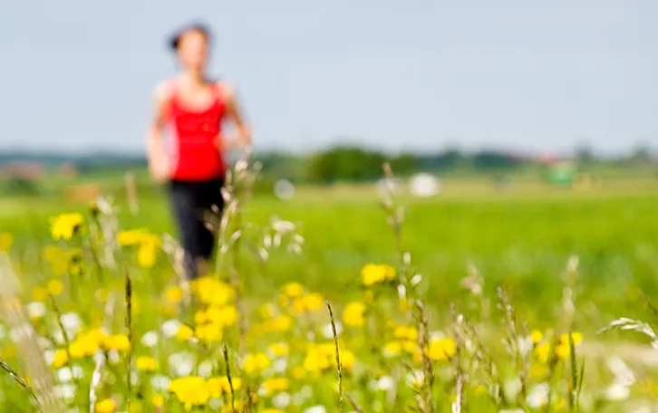Eine blühende Wiese und eine verschwommene laufende Person im Hintergrund