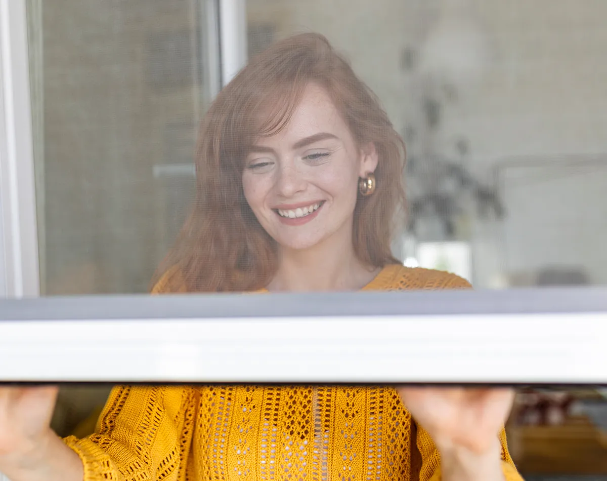 Tipps zur Linderung Pollenschutzfenster Eine Frau hinter einen halb geöffnetem Fenster