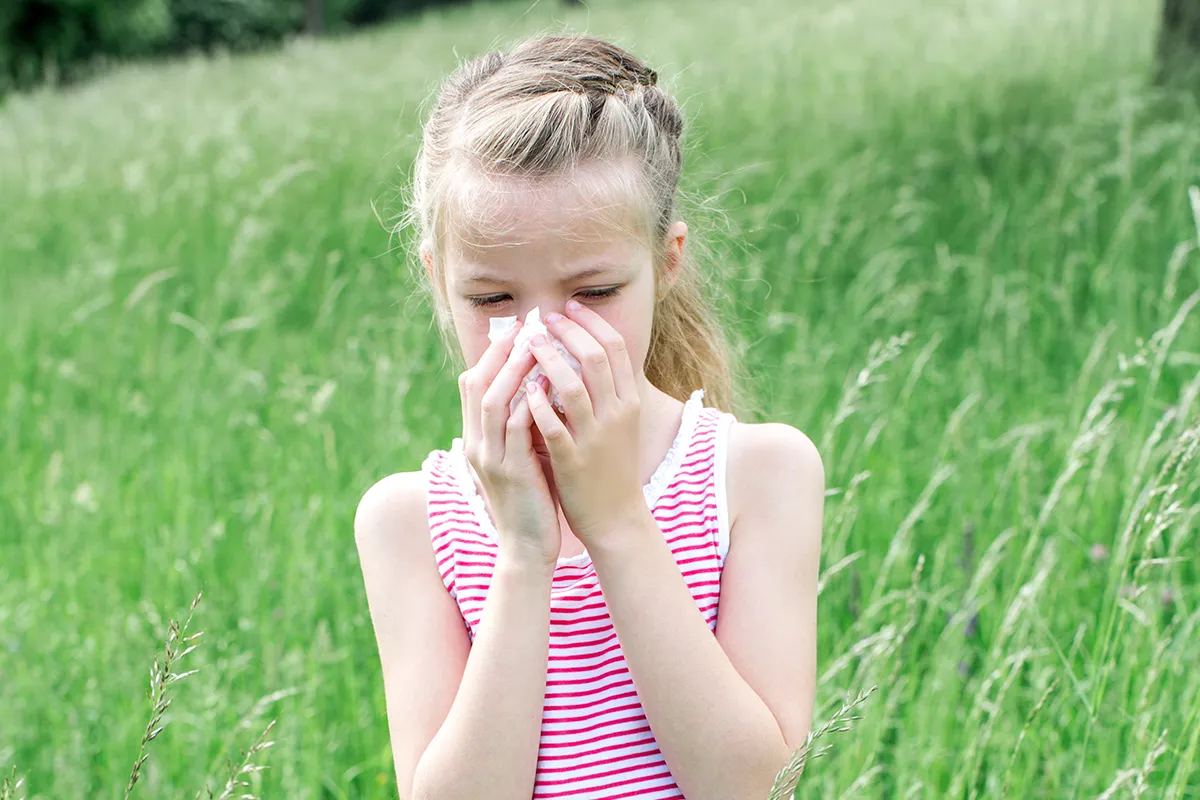 Ein Mädchen auf einer Wiese stehende putzt sich die Nase mit einem Taschentuch