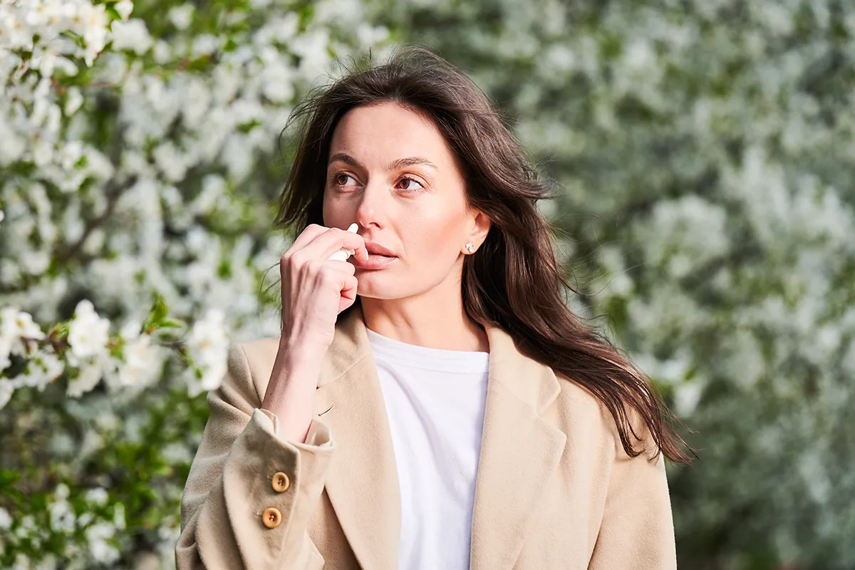 Eine Frau verwendet ein Nasespray vor einer blühenden Pflanze