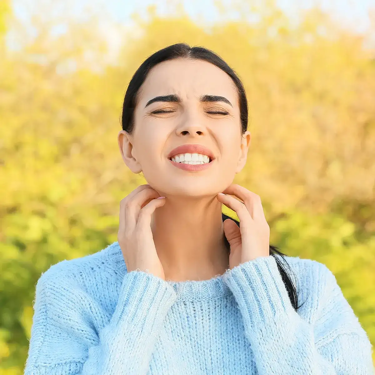 Frau in der Natur mit geschlossenen Augen kratzt sich mit beiden Händen am Hals