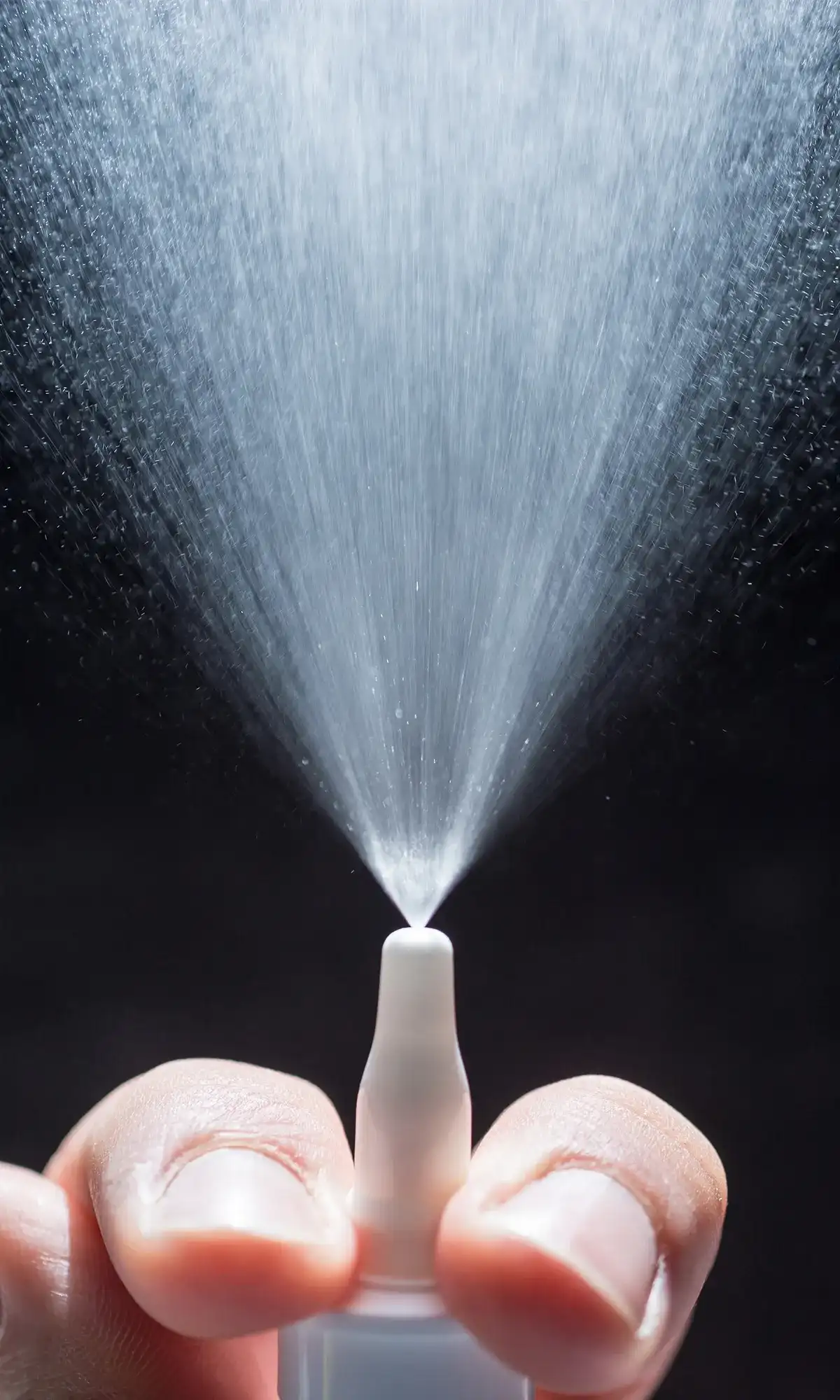 Nasenspray Sprühstoß in die Luft vor dunklem Hintergrund