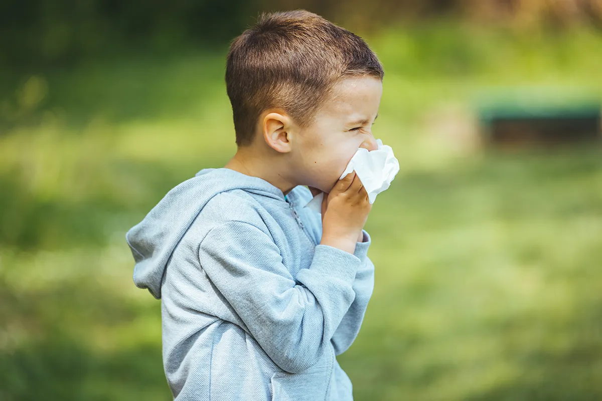 Was ist Heuschnupfen Ein Kind putzt sich auf einer Wiese die Nase